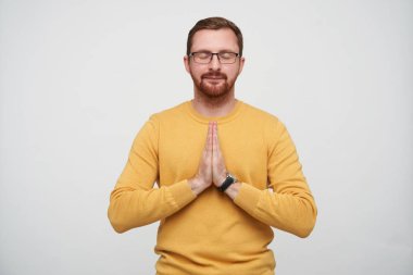 Sakin, genç, esmer, gözlüklü, sakallı bir erkek. Gözlerini kapalı tutarken, dua ederken ellerini katlıyor, beyaz arka planda, gündelik kıyafetlerle dikiliyor.