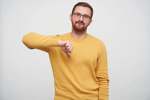 Studio photo of handsome young brunette bearded guy in glasses showing down with thumb and looking at camera with folded lips, isolated over white background — Stock Photo, Image