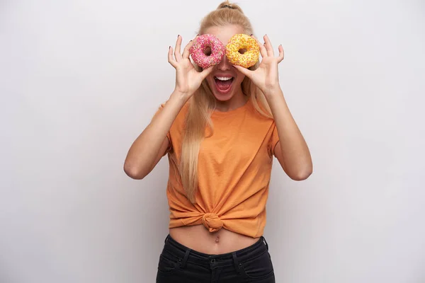 Joyous jovencita rubia rubia de pelo largo y delgada follando mientras estaba de pie sobre fondo blanco, mirando la cámara a través de burros de colores y reír alegremente con la boca ancha abierta. — Foto de Stock