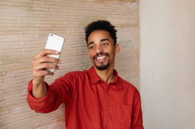 Genç, yakışıklı, kısa saçlı, koyu tenli, kameraya gülümseyen ve evin içinde fotoğraf çeken adamın kapalı çekimleri.