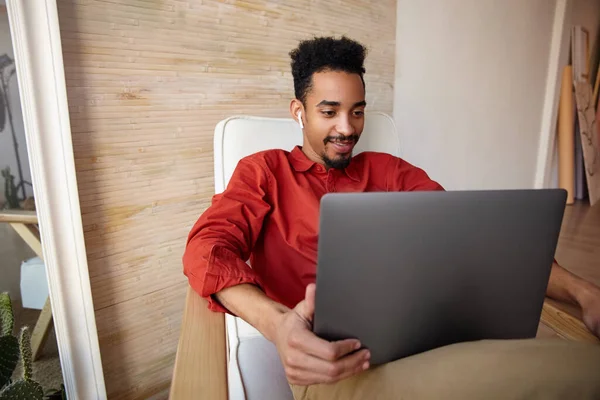 积极的年轻 漂亮的短头发 黑皮肤的生意人 带着现代笔记本电脑走出办公室 身穿红衫 坐在家里的椅子上 — 图库照片