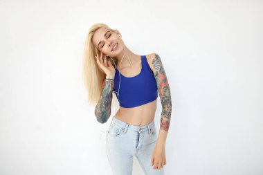 Güzel, genç, zayıf, uzun saçlı, gözlerini kapalı tutarak kulaklıklarıyla müzik dinleyen, güzel gülümseyen, beyaz arka planda soyutlanmış bir kadın.