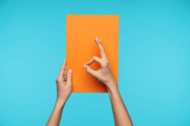 Stüdyoda, güzel bir kadının ellerinin sarı bir kağıt parçasını kaldırdığı ve mavi arka planda duran el hareketlerini muhafaza ettiği fotoğraf.