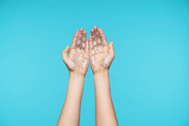 Çekici bir bayanın elleri avuçlarını birbirine gösterirken, üzerinde parıltılar varken mavi arka planda poz verirken ellerini yıkarken.