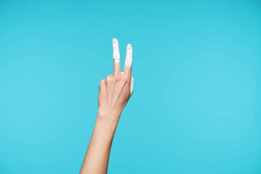 Kadının zarif el şekli iki parmakları vücut dilinde, kaldırılmış parmaklarında beyaz boya, mavi arka planda poz veriyor.