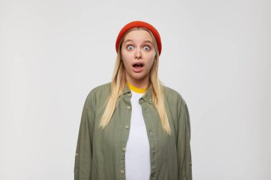 Meşgul, beyaz saçlı, sıradan saç stili olan, geniş gözleri ve ağzı açık, mavi arka planda izole bir şekilde kameraya bakan genç ve çekici bir kadın.