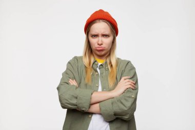 Genç, güzel, beyaz saçlı bir bayanın mavi arka planda dikilirken ellerini göğsüne koyup dudaklarını büzüştürmesi ve ellerini çaprazlamasına gücendi.