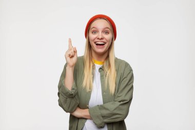 Heyecanlı, genç, beyaz saçlı, işaret parmağını kaldıran bir kadın fikri olduğu için sevinçle kameraya bakıyor ve mavi arka planda duruyor.