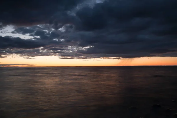 Sunset over the swedish southern coast with rainclouds and rain on the horizon