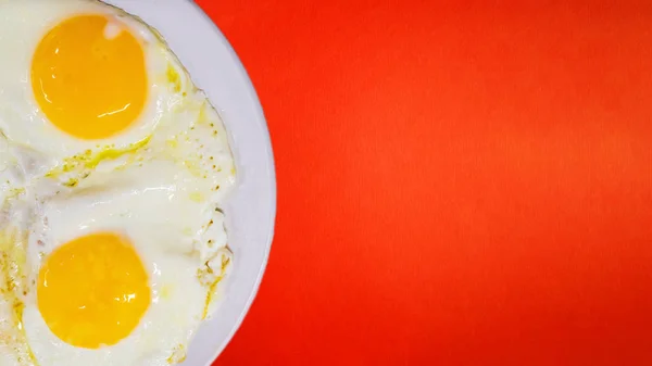 Fried eggs from two eggs close-up on a light plate, on a red background. The concept of fun food.Children\'s fun food, breakfast.