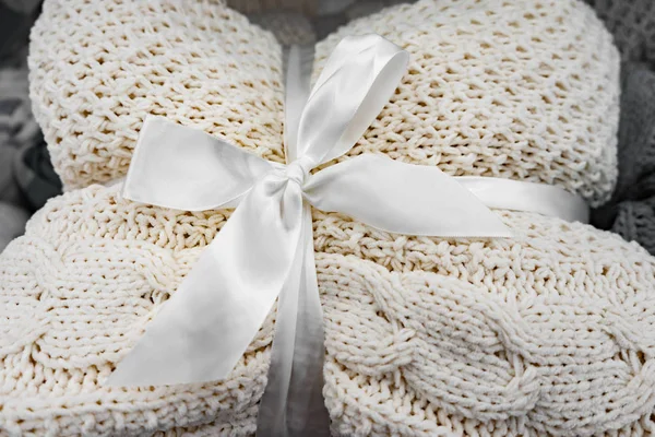A soft knitted blanket is folded and tied with a white ribbon with a bow. The concept of comfort and coziness. Gift for the holiday.