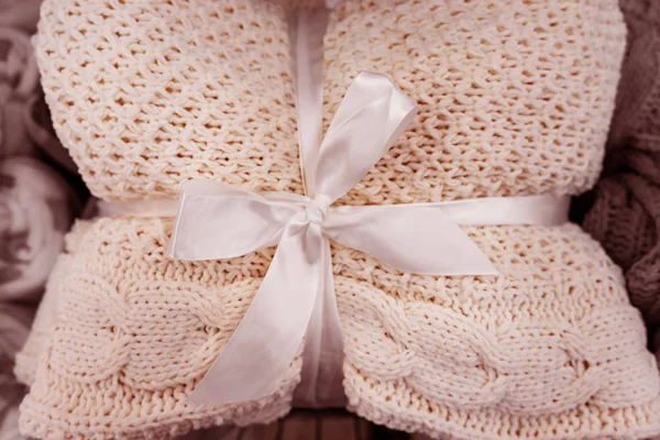 A soft knitted blanket is folded and tied with a white ribbon with a bow. The concept of comfort and coziness. Gift for the holiday.