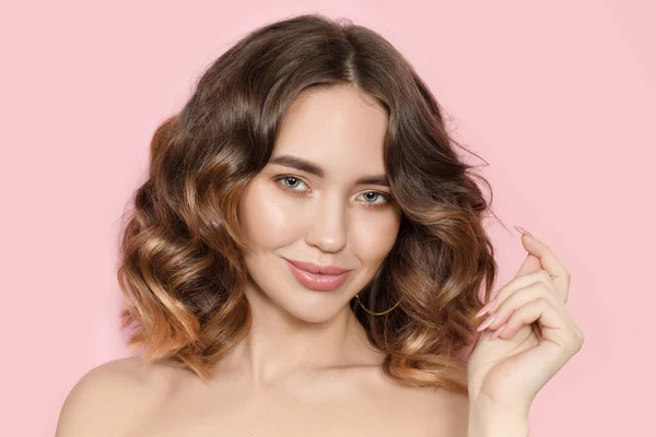 Pembe arka planda gülümseyen kıvırcık saçlı esmer kadın..