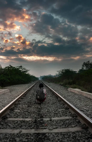 Çantalı çocuk tren raylarında oturmuş yola bakıyor. Telifsiz Stok Fotoğraflar