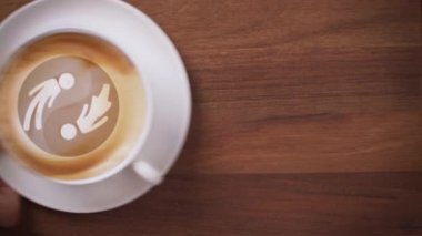 Erkek, yin yang latte sanatıyla kahve servisi yapan bir elin üst görüntüsü.