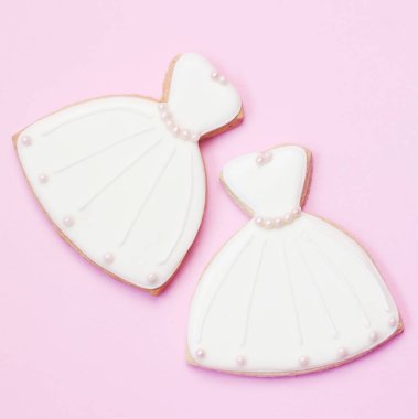 Pembe arka planda gelinlik şeklinde beyaz kurabiyeler.