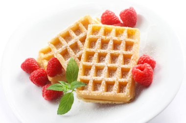 Beyaz tabakta tozlu waffle ve ahududu.
