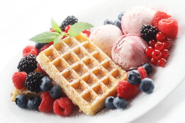 Waffle, dondurma ve beyaz tabakta karışık meyveli tatlı.