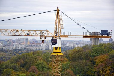 İnşaat vinci. Gökyüzüne karşı inşaat vinci. Doğayla çevrili kentsel binaların arka planında inşaat vinci.