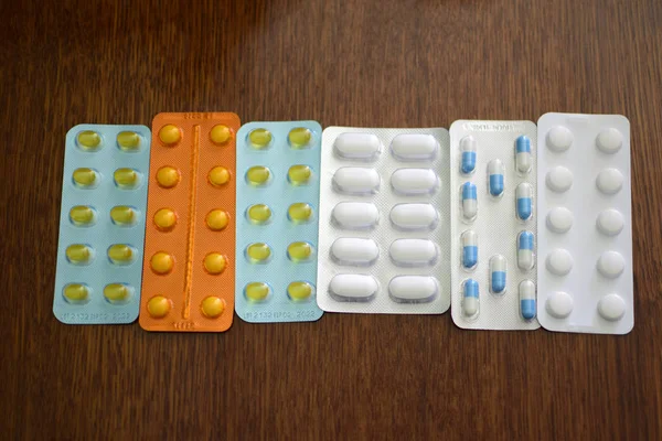 ブリスターパックの錠剤の山 ブリスターパックの多色薬がいっぱいです 木製の背景に閉じます オレンジ 白の錠剤パッケージ 薬のブリスターパック錠剤入り錠剤のパック — ストック写真