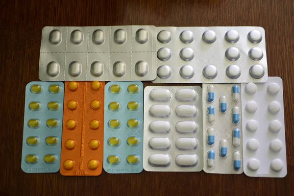 A pile of pills in blister packs. Blister packs full of multi-colored pills. Close up on wooden background. Blue, orange, white pills package. Pharmaceutical blister pack. Pack of pills with tablets.