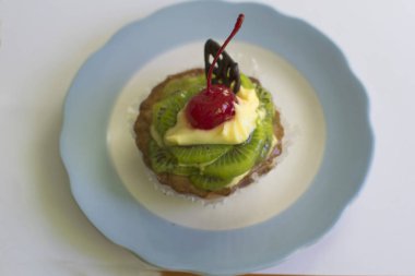 Krema ve kirazlı kek sepeti mavi bir tabakta. Kivili renkli meyveli kekler, kiraz şekeri, krema ve çikolata..