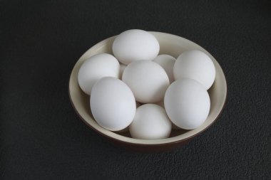 Beyaz organik tavuk yumurtaları siyah arka planda bir tabağa konur.