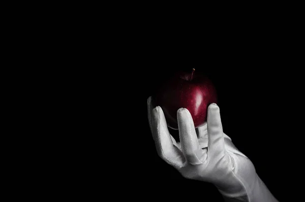 female hand in a long white glove holds a red apple