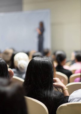 Seyirciler sunumu izliyor. Sahnedeki kadın sunucu kalabalığa konuşma yapıyor. Yatırımcı konferansında kadın konuşmacı. Konferans sırasında bulanık sunucu bulanıklığı.