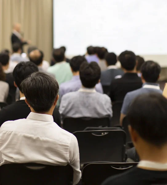 Conference photo audience and speaker giving speech. Seminar presenter on a panel during forum. Corporate manager in sales executive training discussion on stage. Investor pitch presentation.