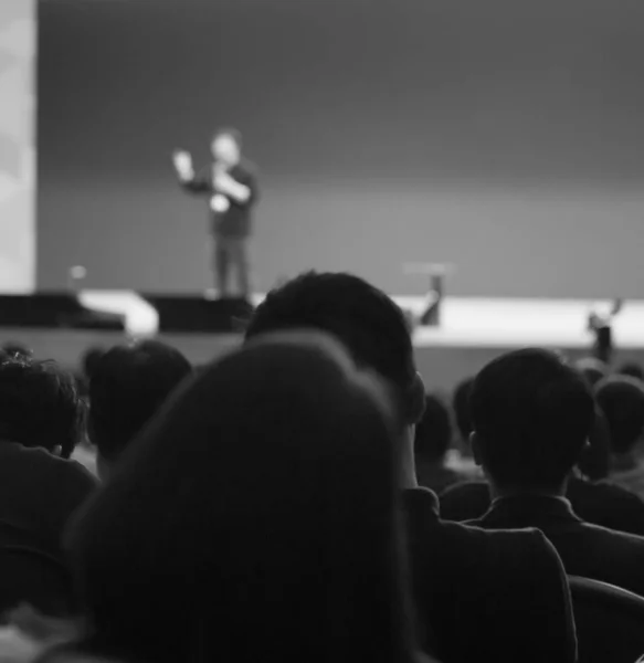 Seminar presenter at corporate conference giving speech. Speaker giving lecture to business audience. Executive manager leading discussion in hall during company training event. Black and white photo