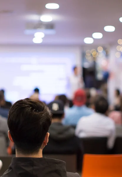 Presenter at corporate conference giving speech. Speaker giving lecture to business audience in seminar. Executive manager leading discussion in hall during company training event.