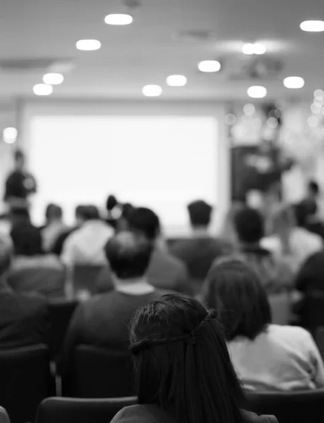 Audience watching a presentation. Presenter on stage giving talk to crowd of people. Speaker at investor pitch conference. Defocused blurred presenter during conference lecture event. Seminar photo.