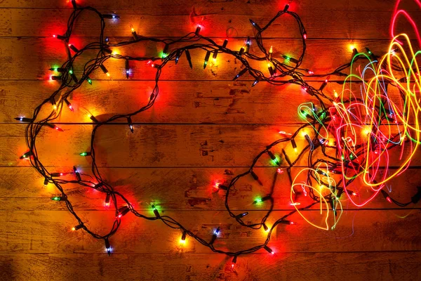 Colorful Christmas garland warm lights. Multicolored light lines. Wooden background. — Stock Photo, Image