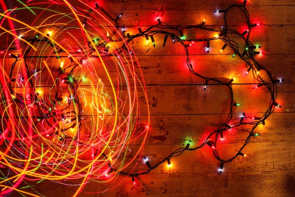 Colorful Christmas garland warm lights. Multicolored light lines. Wooden background. — Stockfoto