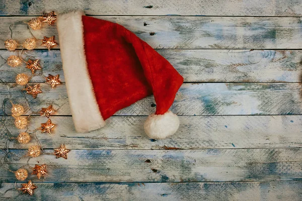 Christmas background with santa hat and christmas lights on rustic vintage wooden background. Garland. — Stock Photo, Image