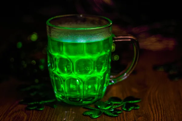 St. Patrick\'s Day Green Beer pint on wooden table, decorated with shamrock leaves. Glass of Green beer close-up. Selective focus. Blurred background. Bokeh.