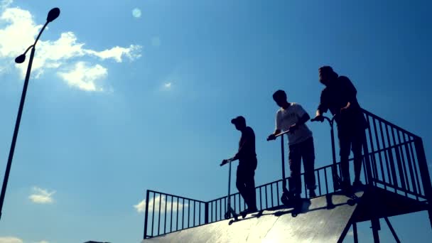 Друзья тусуются в скейт-парке в летний день, пока мальчик садится на электрошокер — стоковое видео