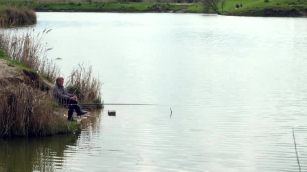 Patiënt visser zit bij het meer te wachten op beten. Vissen. Bewolkte herfstdag — Stockvideo