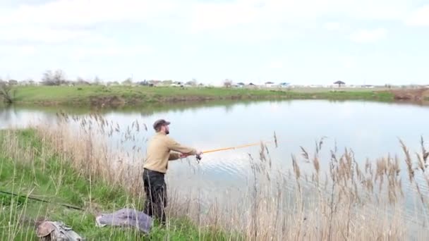 Рибалка тримає в руках вудку, що стоїть на березі озера Осінній день — стокове відео