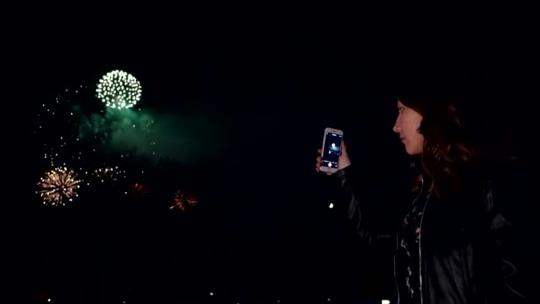 Menina à noite olha para os fogos de artifício no céu e fazer um vídeo no smartphone . — Vídeo de Stock