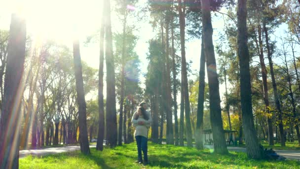 Пара закоханих стоїть в парку і обіймається в одному одязі. Сонячне світло, великі дерева — стокове відео