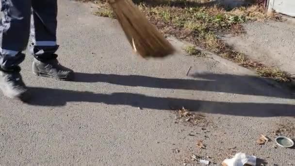 Woźny zamiatający liście na ulicy. Miotła czyści asfalt. Zamknij się. — Wideo stockowe
