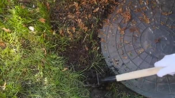 The gardener loosens the ground in the garden around the manhole — Stock Video