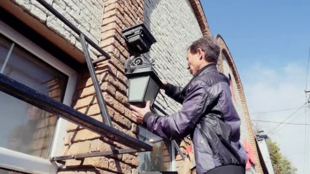 Eletricista em pé na escada e mudar a lâmpada na lâmpada de fachada da casa — Vídeo de Stock