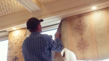 Cırt cırt bağlayıcıyı söken erkek işçi odadaki büyük pencerenin perdelerini kapatıyor.