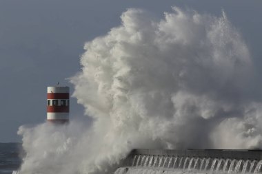 Büyük dalga sıçraması ve püskürtme. Kuzey Portekiz sahil iskelesi ve deniz feneri.