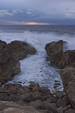 Yağmur ve fırtınadan önce gün batımında deniz kayalıkları. Kuzey Portekiz kayalık kıyıları.