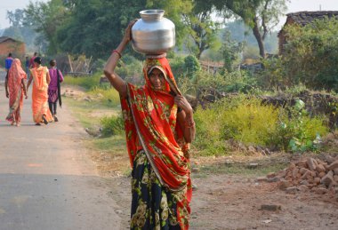 Tikamgarh, Madhya Pradesh, Hindistan - 12 Kasım 2019: Kimliği belirsiz bir yerli köylü kadın geleneksel çömleklerde kafalarında su taşıyor,.