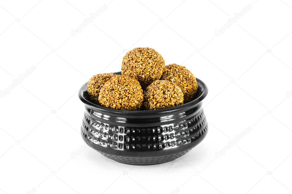 Sesame seed ball or tilgul laddo in black bowl isolated on white background. Indian festival makar sankranti concept.